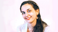 Dr. Clio Agrapidis mit Ohrring und weißer Kleidung, lächelt leicht zur Seite.